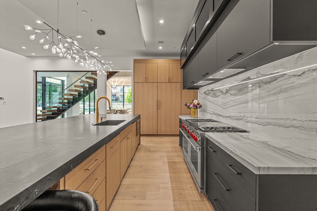 kitchen with pendant lighting, light brown cabinets, range with two ovens, sink, and a center island with sink