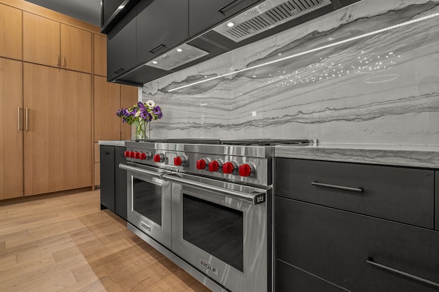 kitchen with double oven range, wall chimney exhaust hood, and light hardwood / wood-style flooring