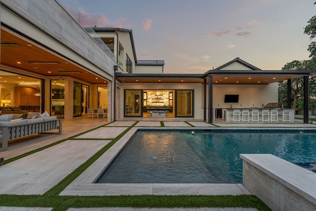 pool at dusk featuring ceiling fan, a patio area, exterior bar, and outdoor lounge area