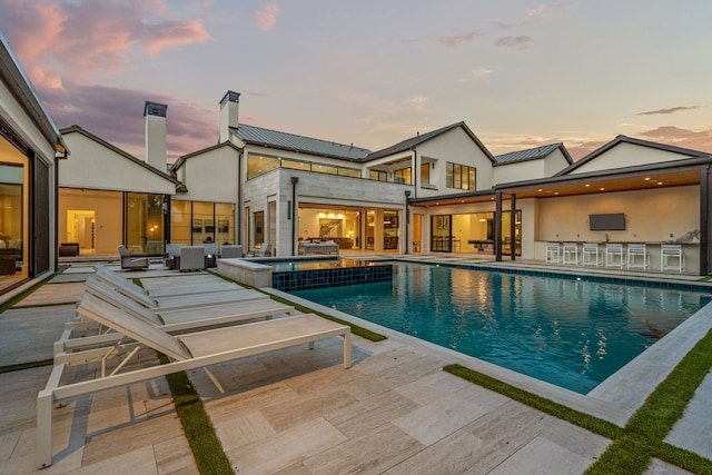 pool at dusk featuring a bar, a patio, and an in ground hot tub