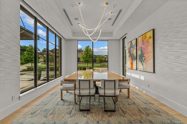 dining area featuring light wood-type flooring, a healthy amount of sunlight, a tray ceiling, and a notable chandelier