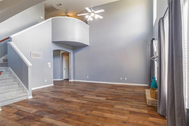 unfurnished living room featuring ceiling fan, dark hardwood / wood-style floors, and a high ceiling