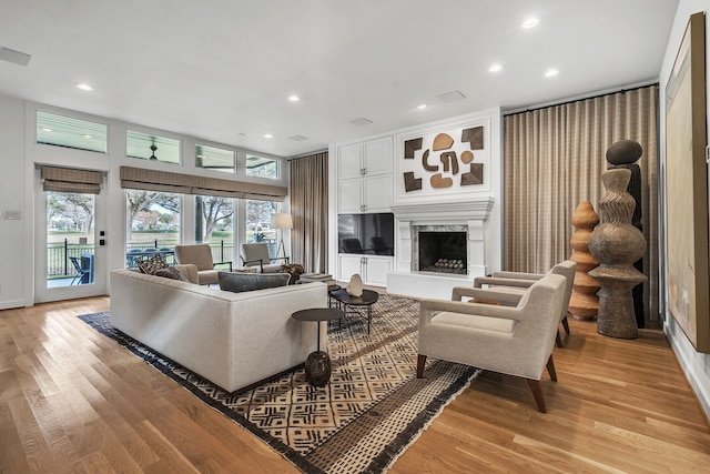 living area with recessed lighting, a fireplace with raised hearth, and light wood-type flooring