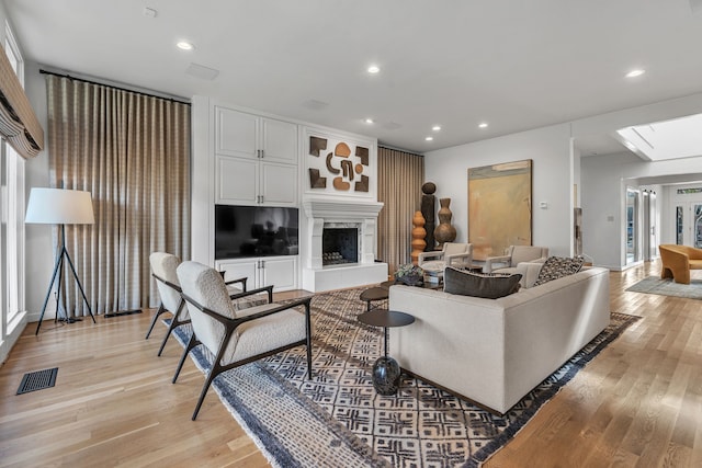 living room featuring a skylight, a fireplace, and light hardwood / wood-style flooring