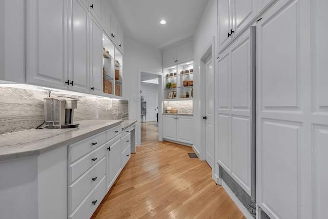 kitchen featuring light wood finished floors, tasteful backsplash, glass insert cabinets, light stone countertops, and white cabinets