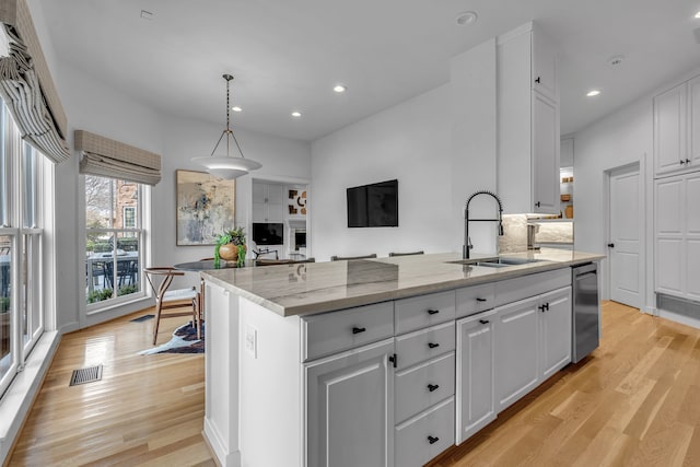 kitchen featuring visible vents, a sink, white cabinetry, light wood-style floors, and light stone countertops