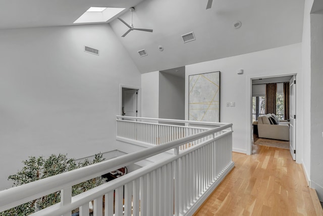 corridor featuring high vaulted ceiling, light hardwood / wood-style flooring, and a skylight