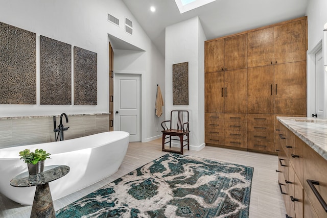 bathroom with vanity, vaulted ceiling with skylight, and a bath