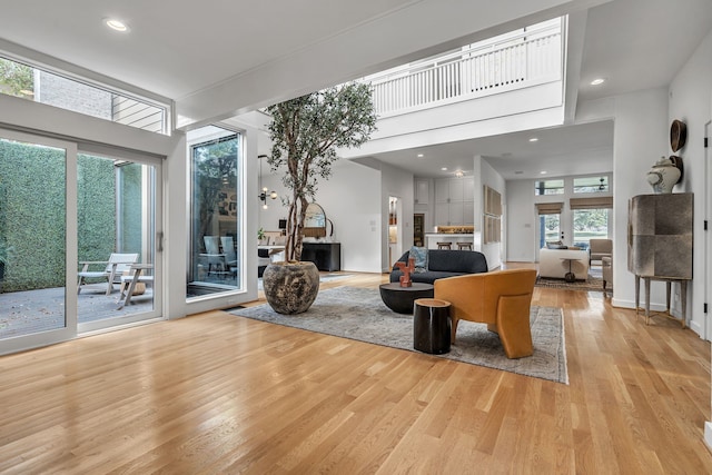 living room with light wood-type flooring, a towering ceiling, and a wealth of natural light