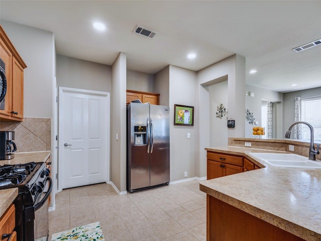 kitchen featuring stainless steel refrigerator with ice dispenser, sink, backsplash, light tile patterned floors, and black range with gas stovetop