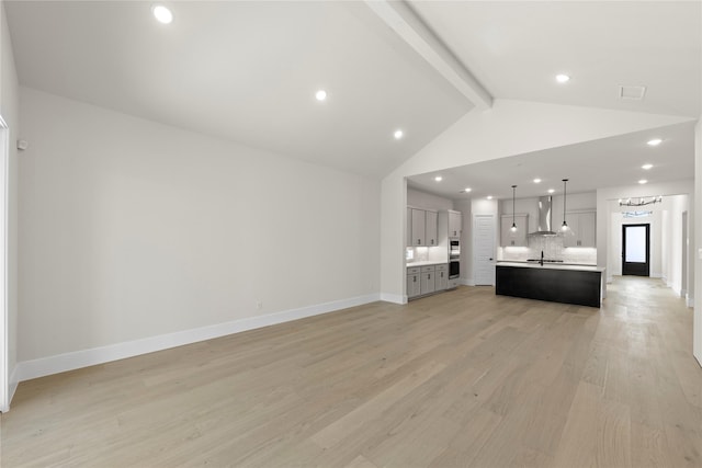 unfurnished living room with visible vents, light wood-style floors, a sink, beamed ceiling, and baseboards