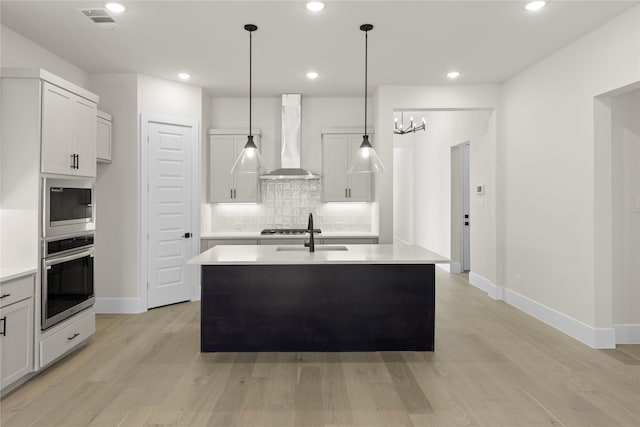 kitchen featuring an island with sink, wall chimney range hood, appliances with stainless steel finishes, and light countertops