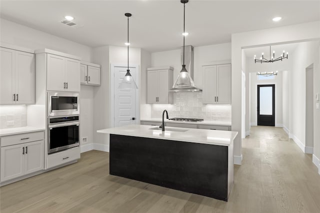 kitchen with a center island with sink, visible vents, wall chimney exhaust hood, stainless steel appliances, and light countertops