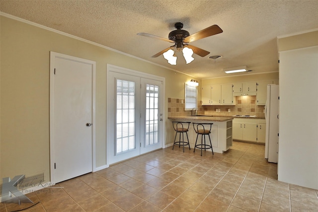 kitchen with kitchen peninsula, decorative backsplash, a kitchen bar, white appliances, and white cabinets