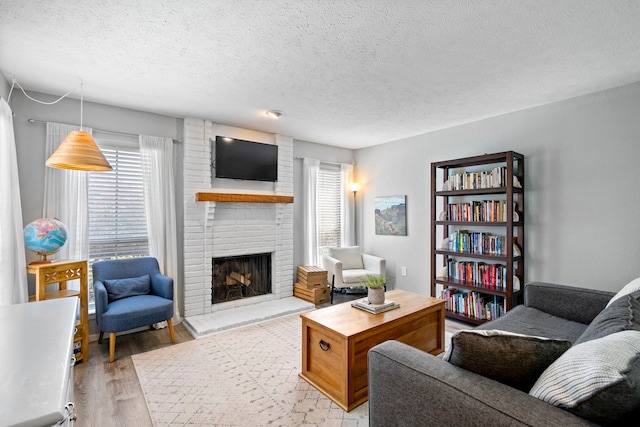 living room featuring a textured ceiling, a brick fireplace, and light wood-type flooring