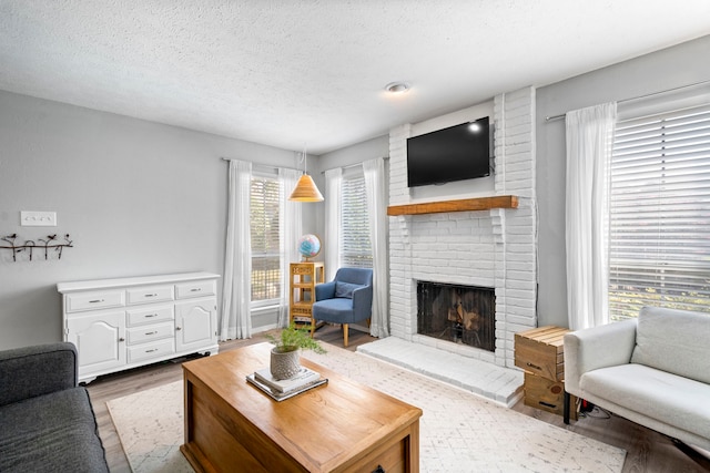 living room featuring a textured ceiling, light wood-type flooring, a healthy amount of sunlight, and a fireplace