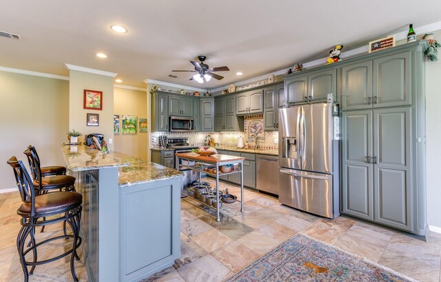 kitchen with ceiling fan, kitchen peninsula, a kitchen breakfast bar, stainless steel appliances, and ornamental molding