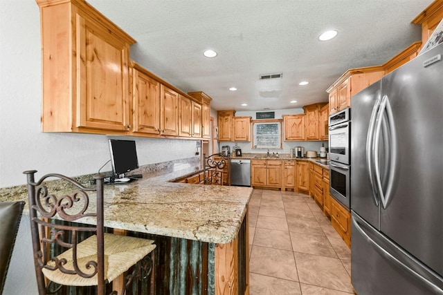 kitchen featuring light stone countertops, appliances with stainless steel finishes, a kitchen breakfast bar, kitchen peninsula, and light tile patterned floors