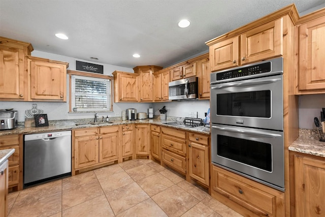 kitchen with light tile patterned flooring, stainless steel appliances, light stone counters, and sink