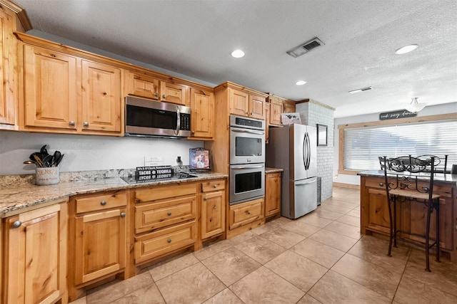 kitchen featuring light stone countertops, light tile patterned floors, appliances with stainless steel finishes, and a textured ceiling