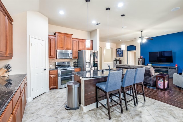 kitchen with appliances with stainless steel finishes, decorative light fixtures, an island with sink, ceiling fan, and a breakfast bar