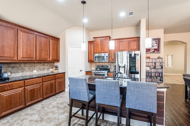 kitchen with appliances with stainless steel finishes, decorative light fixtures, tasteful backsplash, a center island with sink, and a breakfast bar area