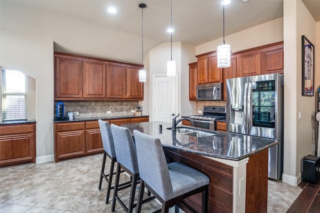 kitchen featuring an island with sink, appliances with stainless steel finishes, tasteful backsplash, dark stone countertops, and sink