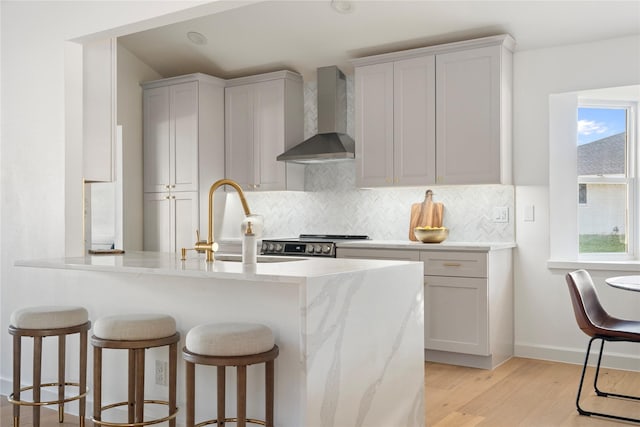 kitchen featuring wall chimney range hood, light hardwood / wood-style floors, sink, decorative backsplash, and stove