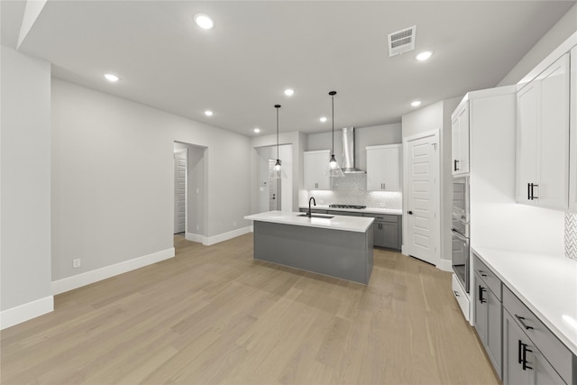 kitchen featuring wall chimney exhaust hood, sink, decorative light fixtures, gray cabinets, and a kitchen island with sink