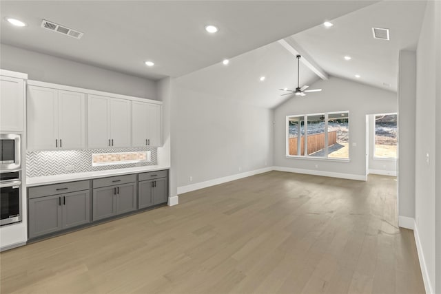 kitchen with appliances with stainless steel finishes, gray cabinetry, backsplash, and light wood-type flooring