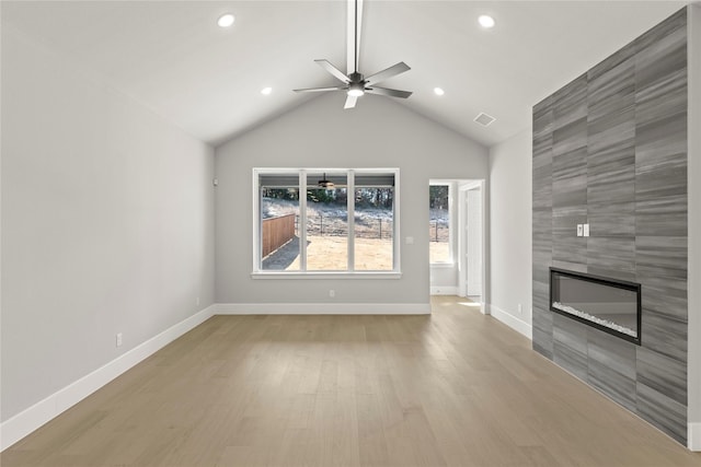 unfurnished living room featuring ceiling fan, lofted ceiling, a tiled fireplace, and light hardwood / wood-style floors