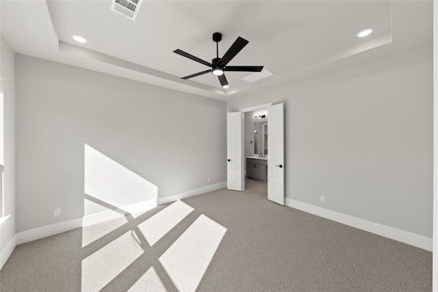 unfurnished bedroom featuring a raised ceiling, ensuite bathroom, carpet flooring, and ceiling fan