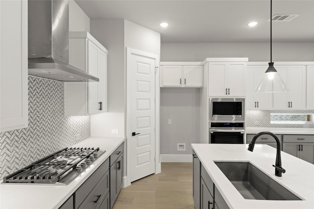 kitchen featuring gray cabinets, pendant lighting, sink, stainless steel appliances, and wall chimney exhaust hood