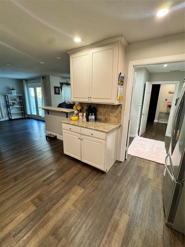 kitchen with dark wood-type flooring, white cabinetry, tasteful backsplash, and stainless steel refrigerator