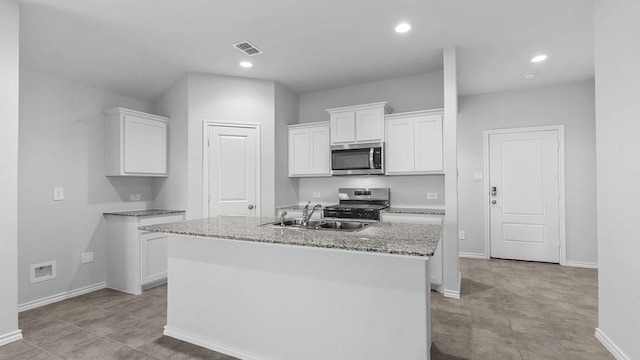 kitchen featuring sink, white cabinetry, a kitchen island with sink, stainless steel appliances, and light stone counters