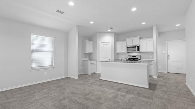 kitchen with appliances with stainless steel finishes, white cabinets, a center island with sink, and light stone countertops