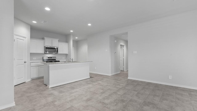 kitchen with white cabinets, appliances with stainless steel finishes, sink, a kitchen island with sink, and light stone counters