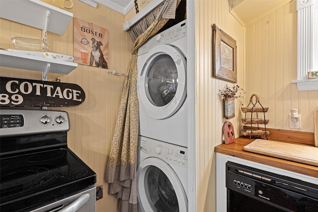 laundry area with ornamental molding, stacked washer / drying machine, and wood walls