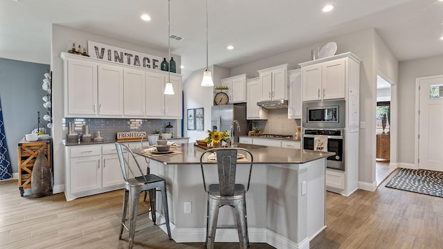 kitchen with a kitchen bar, stainless steel appliances, a kitchen island with sink, hanging light fixtures, and white cabinets