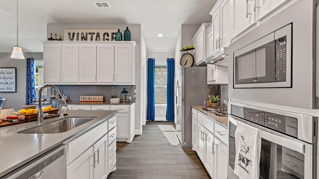 kitchen with white cabinetry, stainless steel appliances, decorative backsplash, decorative light fixtures, and sink