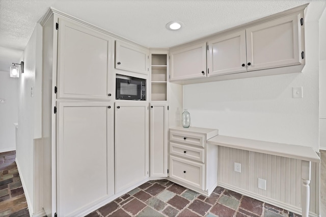 kitchen featuring a textured ceiling, black microwave, and built in desk