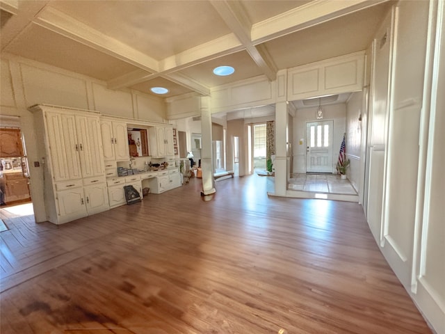 unfurnished living room with beam ceiling, ornate columns, coffered ceiling, and light hardwood / wood-style flooring