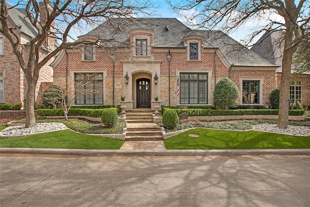 french country home featuring brick siding, stone siding, and a high end roof