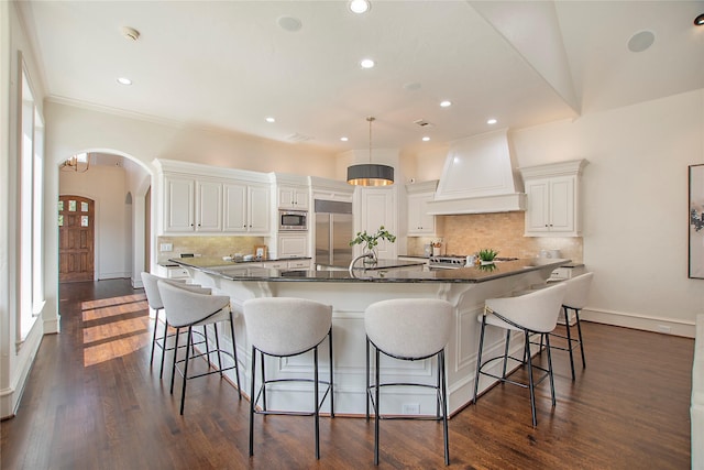 kitchen featuring a kitchen bar, dark wood-type flooring, arched walkways, built in appliances, and custom exhaust hood