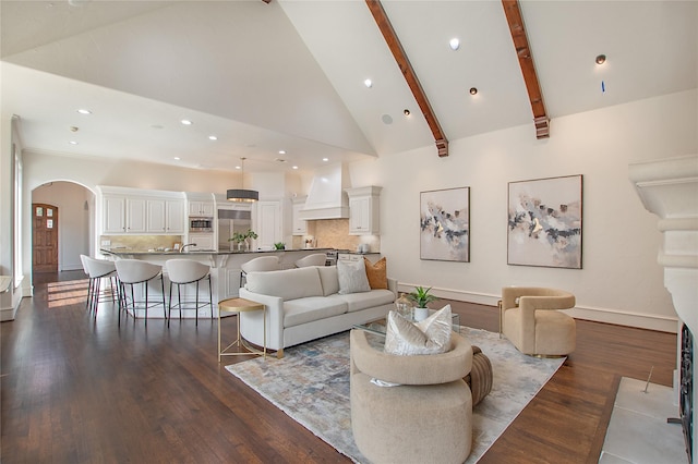 living room with dark wood-style floors, baseboards, high vaulted ceiling, arched walkways, and beamed ceiling