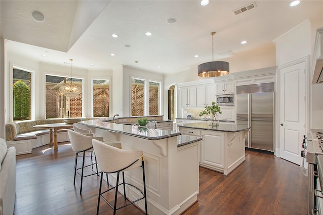 kitchen with visible vents, crown molding, built in appliances, a large island with sink, and dark wood-style floors