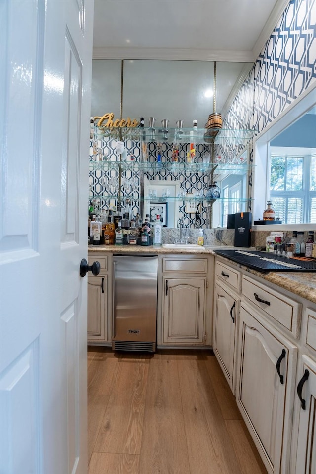 bar featuring light hardwood / wood-style floors, fridge, sink, ornamental molding, and cream cabinetry