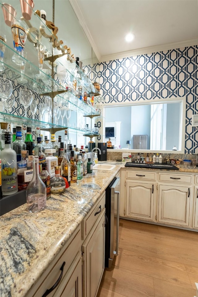 kitchen with light stone countertops, sink, ornamental molding, light hardwood / wood-style flooring, and cream cabinetry