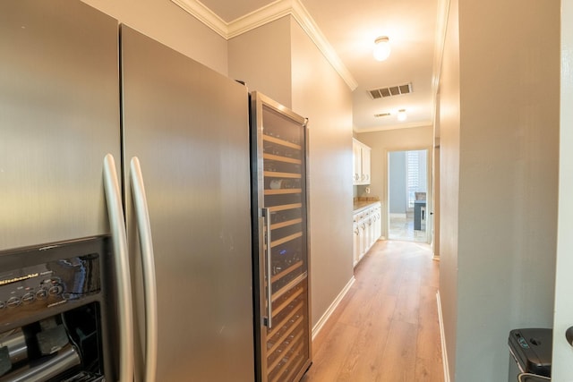 kitchen with stainless steel fridge, white cabinets, crown molding, and light wood-type flooring