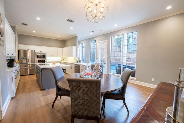 dining room featuring a notable chandelier, sink, crown molding, and light hardwood / wood-style floors